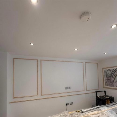 Wall panelling part-built: bare timber mouldings set out on a white wall before painting