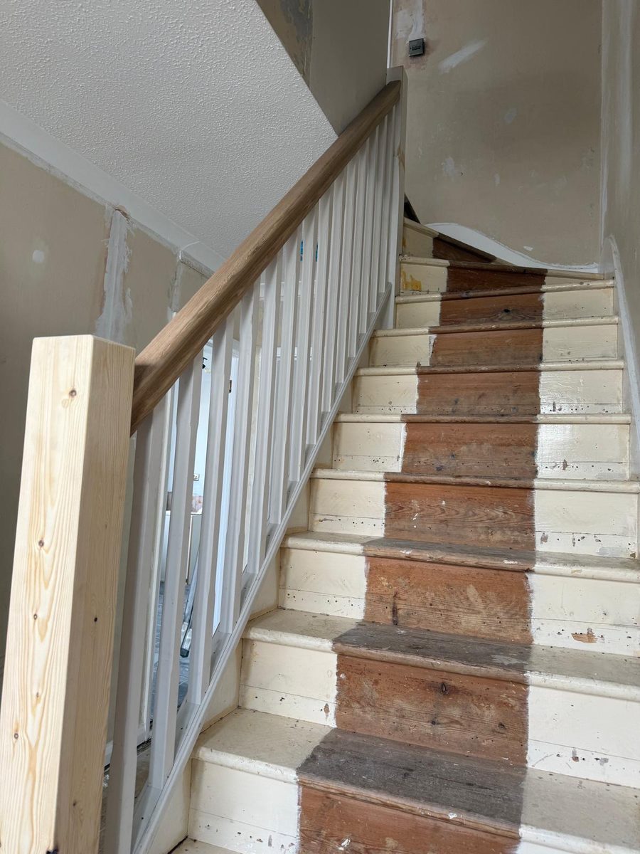 Staircase part-way through a refit, with a new oak-topped handrail, spindles and newel post fitted and the treads still stripped back
